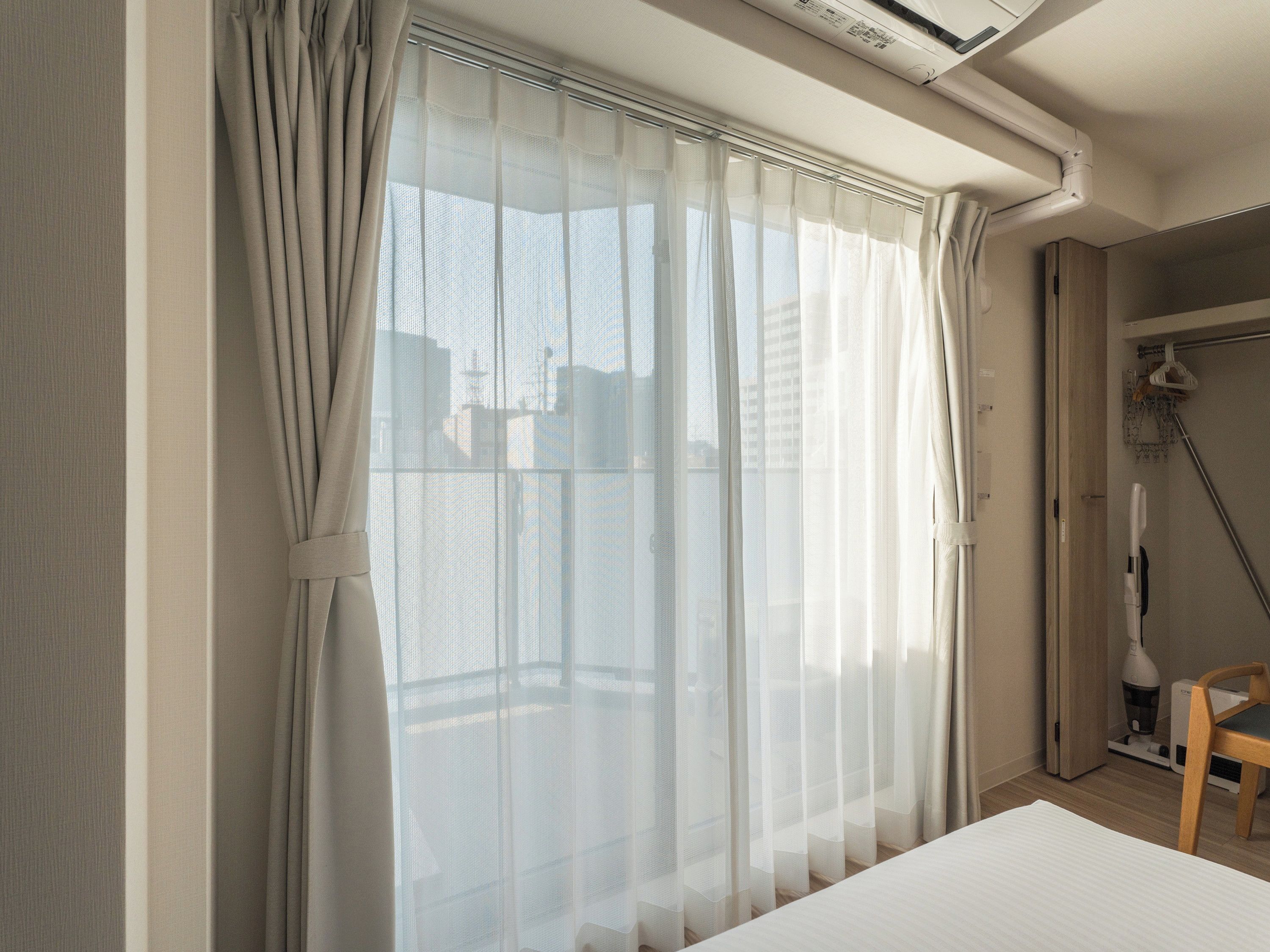 A room with a bed, a shower, and a window with sheer curtains.