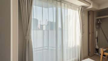 A room with a bed, a shower, and a window with sheer curtains.
