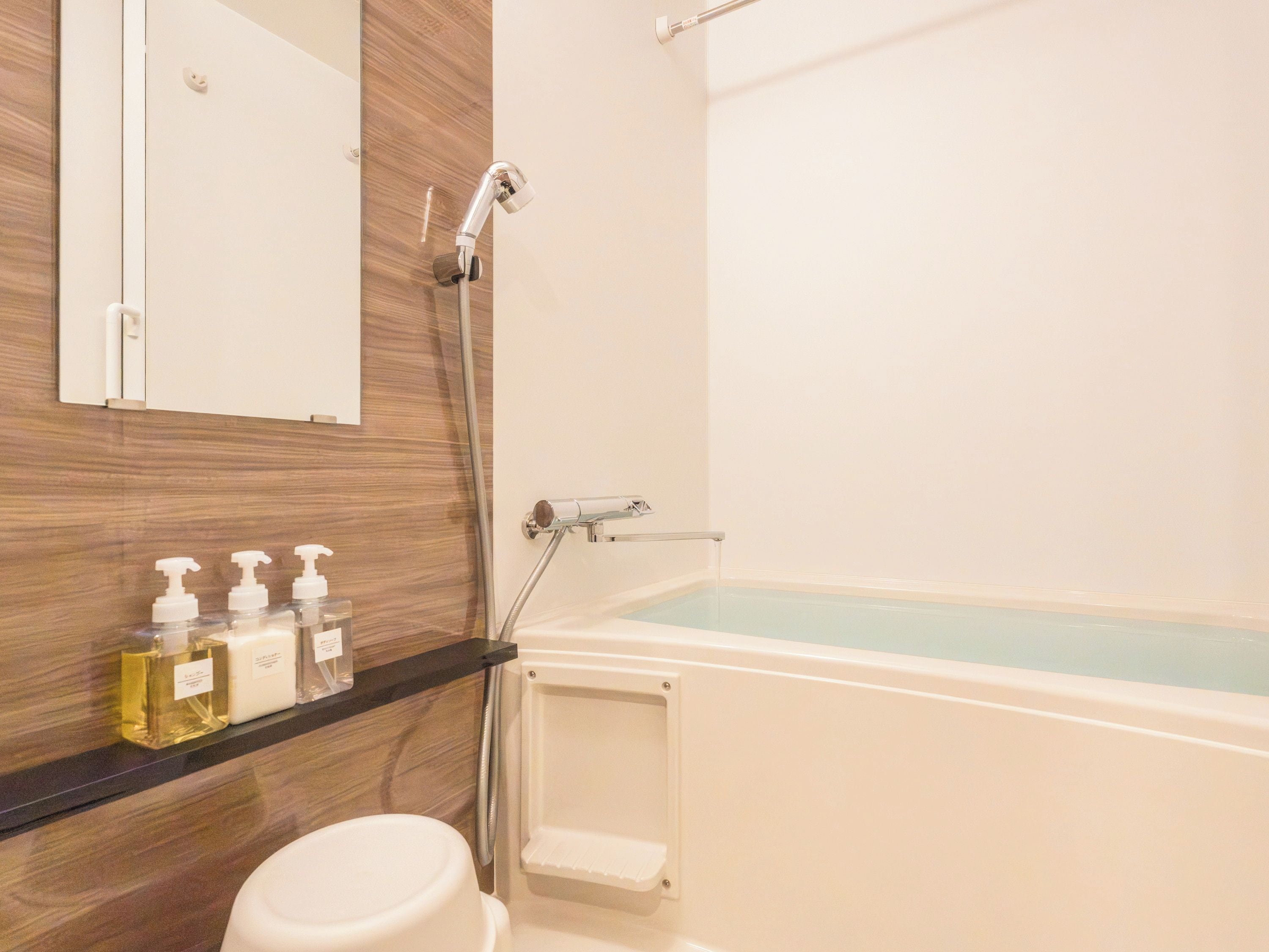 A bathroom with a bathtub, a toilet, a shower, and a shelf with toiletries.