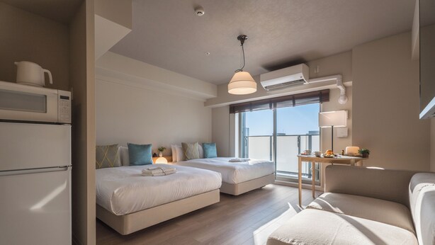 A modern hotel room with a kitchenette, two beds, a sofa, and a balcony with a view. - ESLEAD HOTEL Namba East (Osaka)