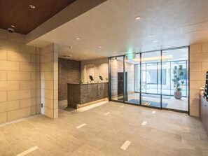 A reception area with a reception desk, a wall-mounted security camera, and a glass door leading to the outside. - ESLEAD HOTEL Namba East (Osaka)