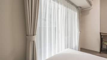 A hotel room with a bed, a chair, and a window with sheer curtains.