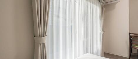 A hotel room with a bed, a chair, and a window with sheer curtains.