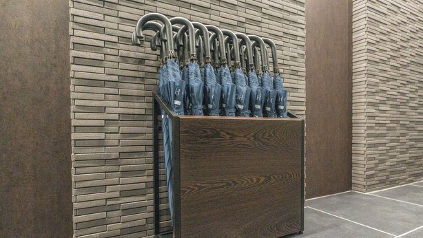 Un espositore di legno con diversi ombrelli appoggiati a un muro in mattoni.