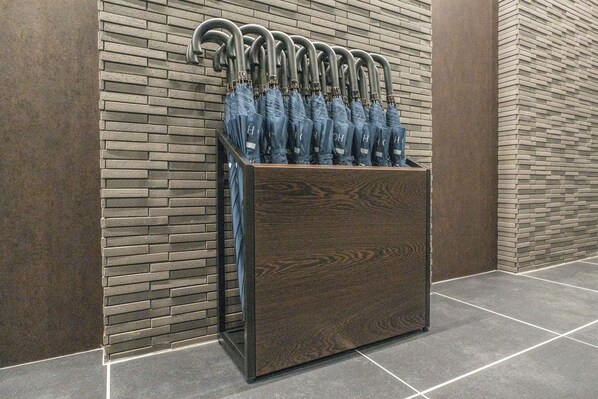 Un espositore di legno con diversi ombrelli appoggiati a un muro in mattoni.