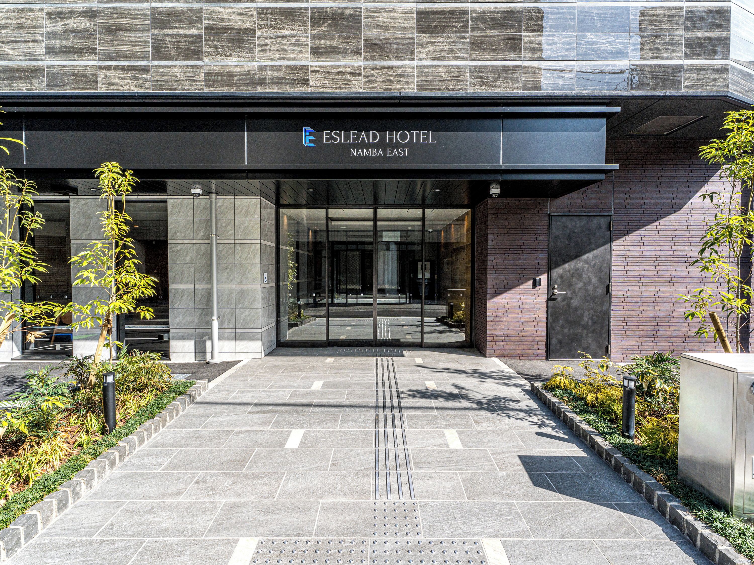 The entrance to the Eslead Hotel in Namibia East with a modern design, featuring a glass door and a paved pathway leading to the entrance.