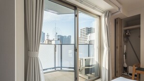 A hotel room with a balcony, a bed, a chair, and a view of the cityscape. - ESLEAD HOTEL Namba East (Osaka)