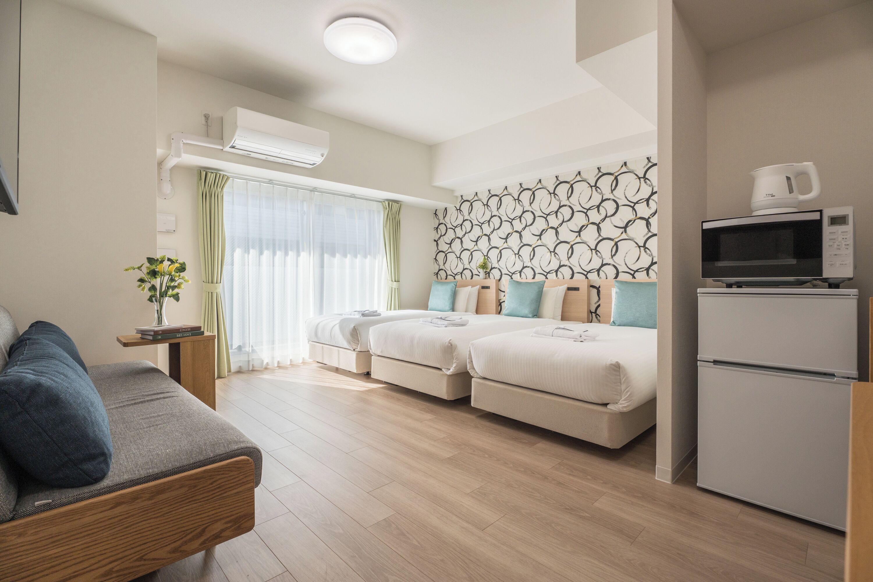 A modern room with a sofa, two beds, a microwave, and an air conditioning unit.