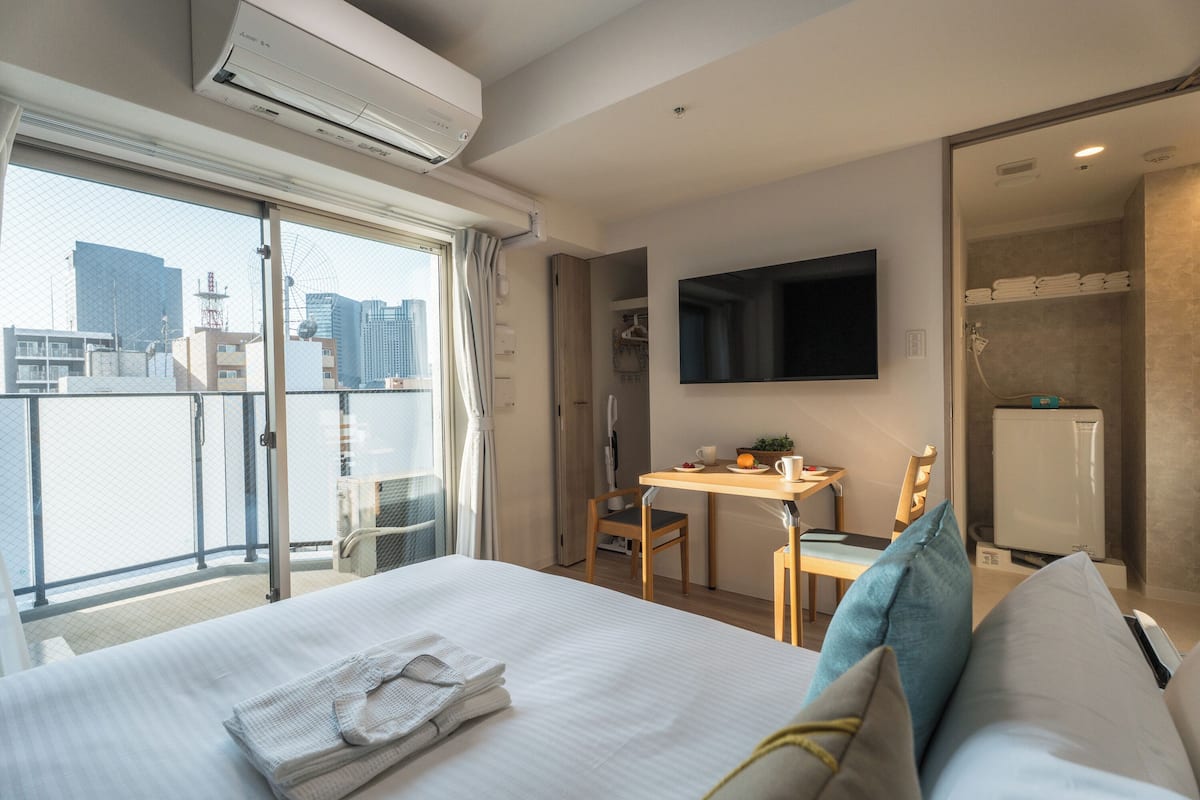 A hotel room with a bed, a desk, a chair, a TV, and a balcony with a city view.