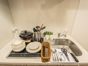 A kitchen counter with a rice cooker, water bottles, a sink, and various utensils. - ESLEAD HOTEL Namba East (Osaka)
