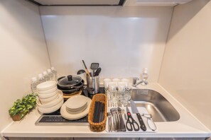 Un piano di lavoro in cucina con piatti e ciotole impilati, un cesto di utensili e un lavandino.