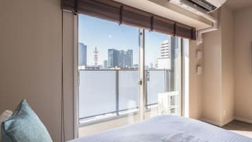 Hotellihuone, jossa on sänky, ikkuna, josta avautuu näkymä kaupunkimaisemaan, ja ilmastointilaite.