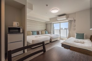 Una camera d'albergo con un letto, una scrivania con un forno a microonde, una sedia, una finestra con tende e un condizionatore d'aria.