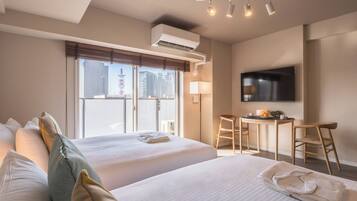 Ein Hotelzimmer mit zwei Betten, einem Schreibtisch, einem Sessel, einem Fernseher und einem Fenster mit Blick auf die Stadt.