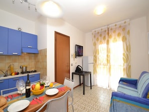 A compact living space with a kitchenette, a dining area, and a sofa. - Comfy Flat With Shared Swimming Pool (San Michele al Tagliamento)
