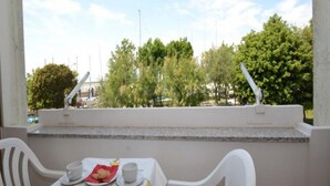 A balcony with a table set for two, chairs, and a view of trees and buildings in the distance. - Comfy Flat With Shared Swimming Pool (San Michele al Tagliamento)