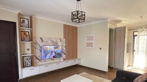 A modern living room with a sofa set, a coffee table, a TV, and a decorative ceiling light. - Charming 1-bedroom apartment with City View in lively Kampala (Kampala)