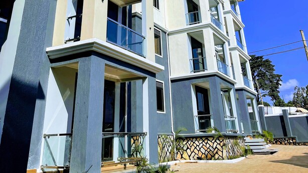 A multi-story residential building with balconies, large windows, and a clear blue sky. - Charming 1-bedroom apartment with City View in lively Kampala (Kampala)