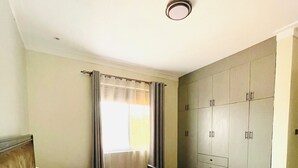 A hotel room with a bed, a wardrobe, and a window with curtains. - Charming 1-bedroom apartment with City View in lively Kampala (Kampala)