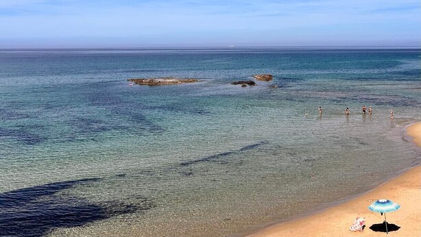 A beach with clear water, a sandy shore, and a few people in the distance. - Affittimoderni Castelsardo - Casa Marittima (Castelsardo)