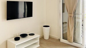 A modern room with a flat-screen TV mounted on the wall, a white console table with black bowls, a tall white vase, and a sliding glass door with beige curtains. - Affittimoderni Castelsardo - Casa Marittima (Castelsardo)