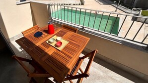A wooden table with chairs on a balcony overlooking a swimming pool and a distant town. - Affittimoderni Castelsardo - Casa Marittima (Castelsardo)