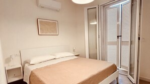 A bedroom with a bed, bedside tables, a hanging light fixture, a framed picture, and a sliding glass door. - Affittimoderni Castelsardo - Casa Marittima (Castelsardo)