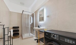Ein modernes Badezimmer mit einer Glasdusche, einem Waschbecken und einer schwarzen Waschmaschine.
