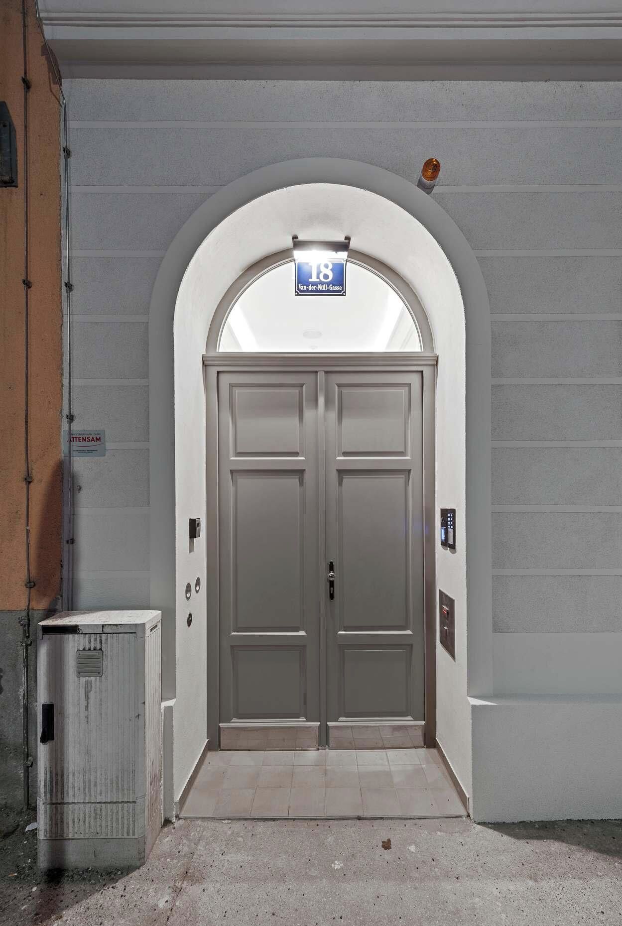 A double door with a sign above it, a utility box to the left, and a wall with horizontal lines.