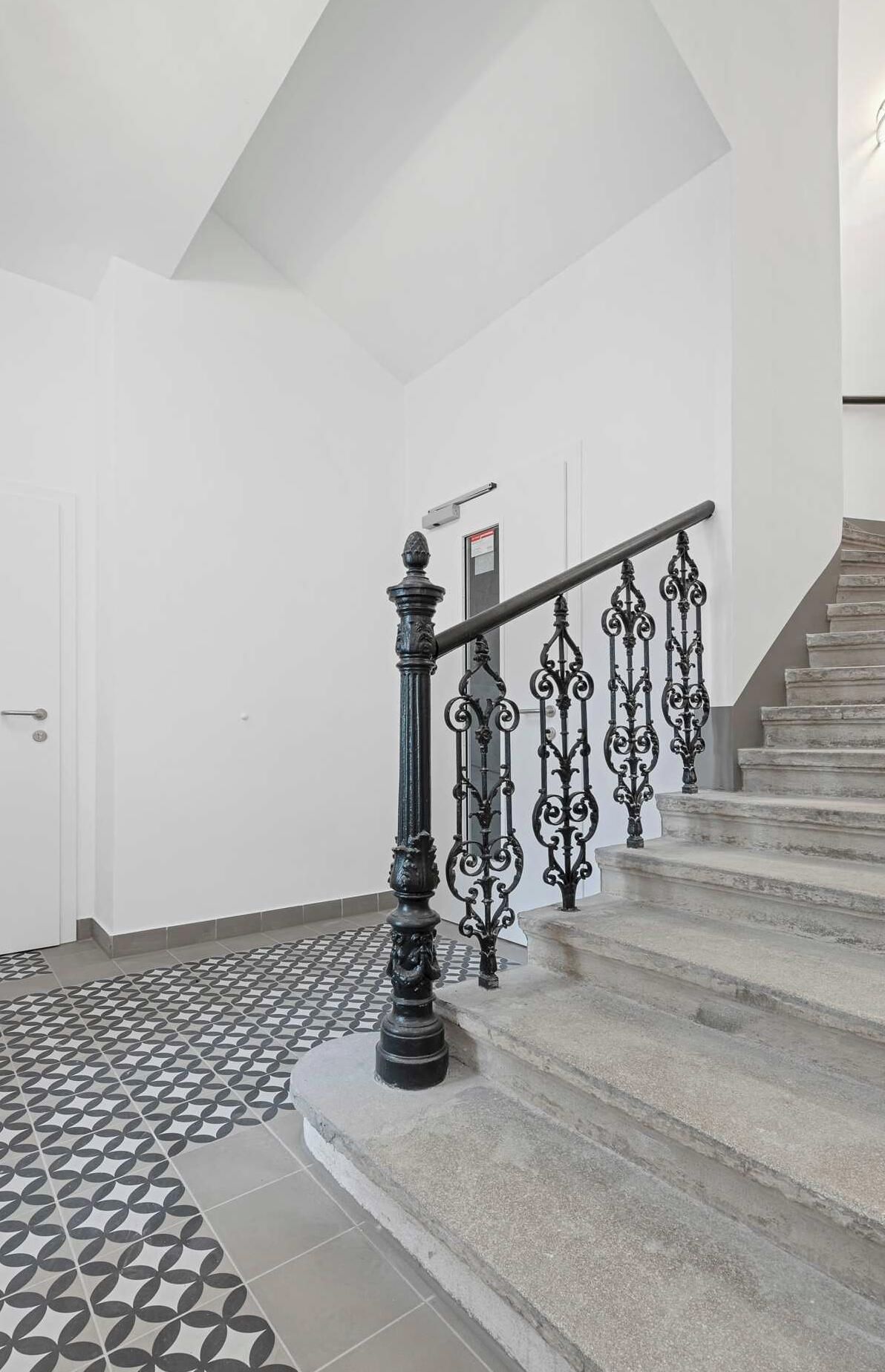 Una escalera con barandillas negras ornamentadas y un suelo con diseño geométrico.