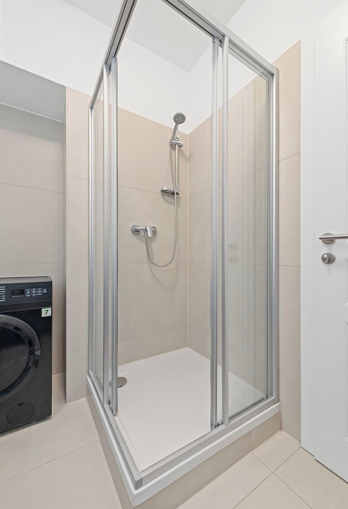 Ducha envuelta en vidrio con cabezal de ducha de mano, grifo empotrado y panel de control.