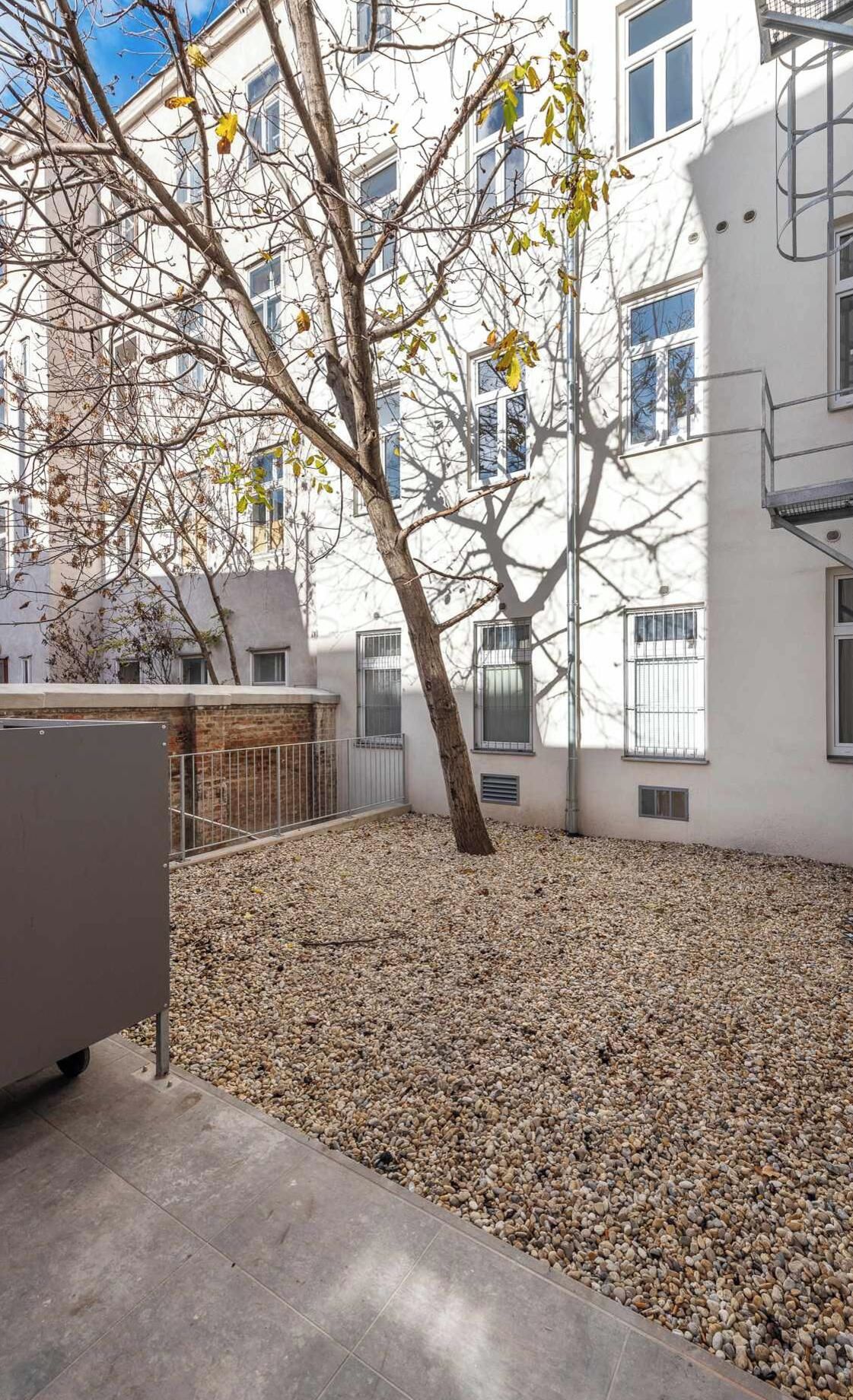A courtyard with a tree, gravel ground, and a building with multiple windows and balconies.