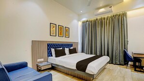 Una habitación de hotel con cama, escritorio, silla, mesita y aire acondicionado.