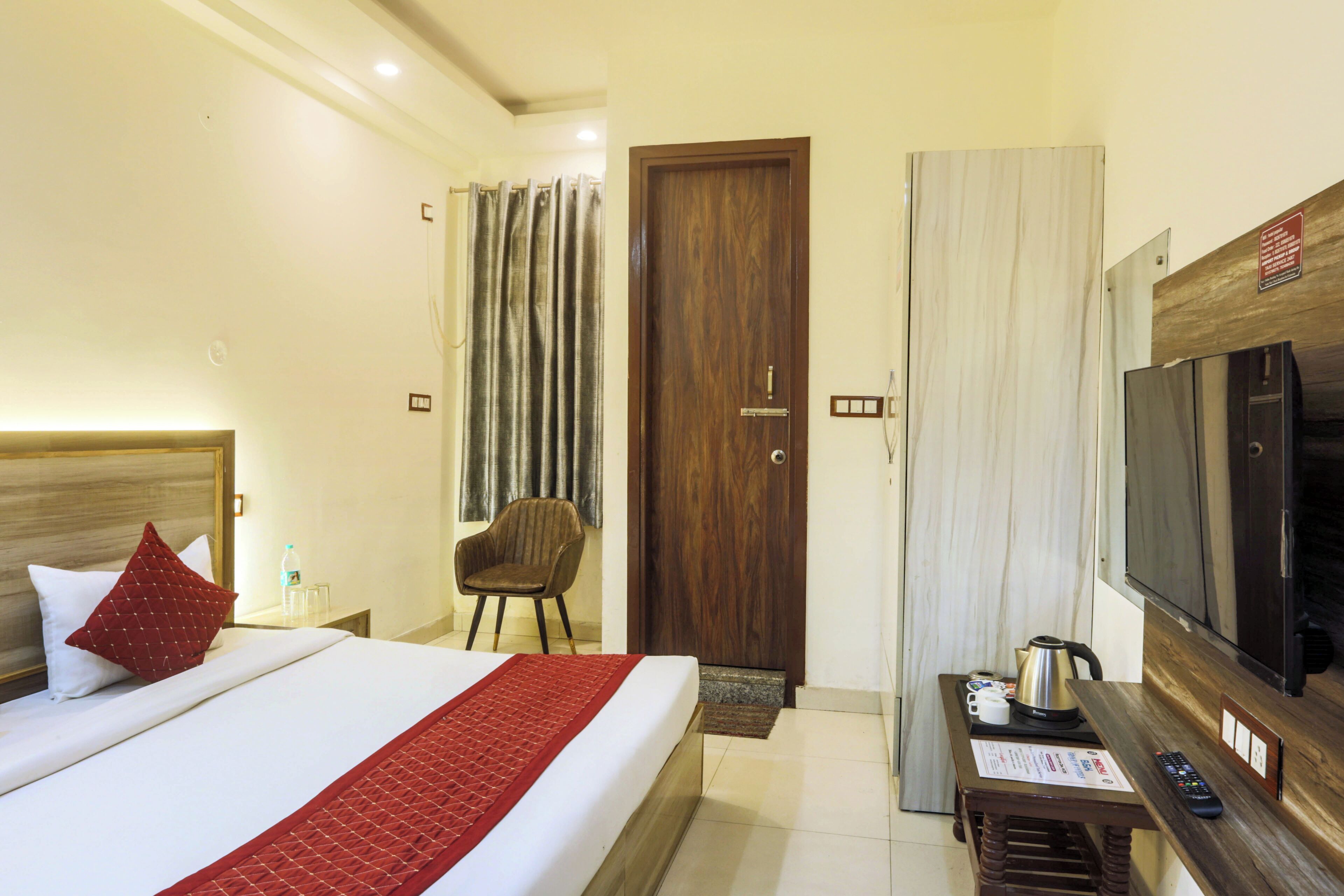 A hotel room with a bed, a chair, a television, and a table with a remote control.