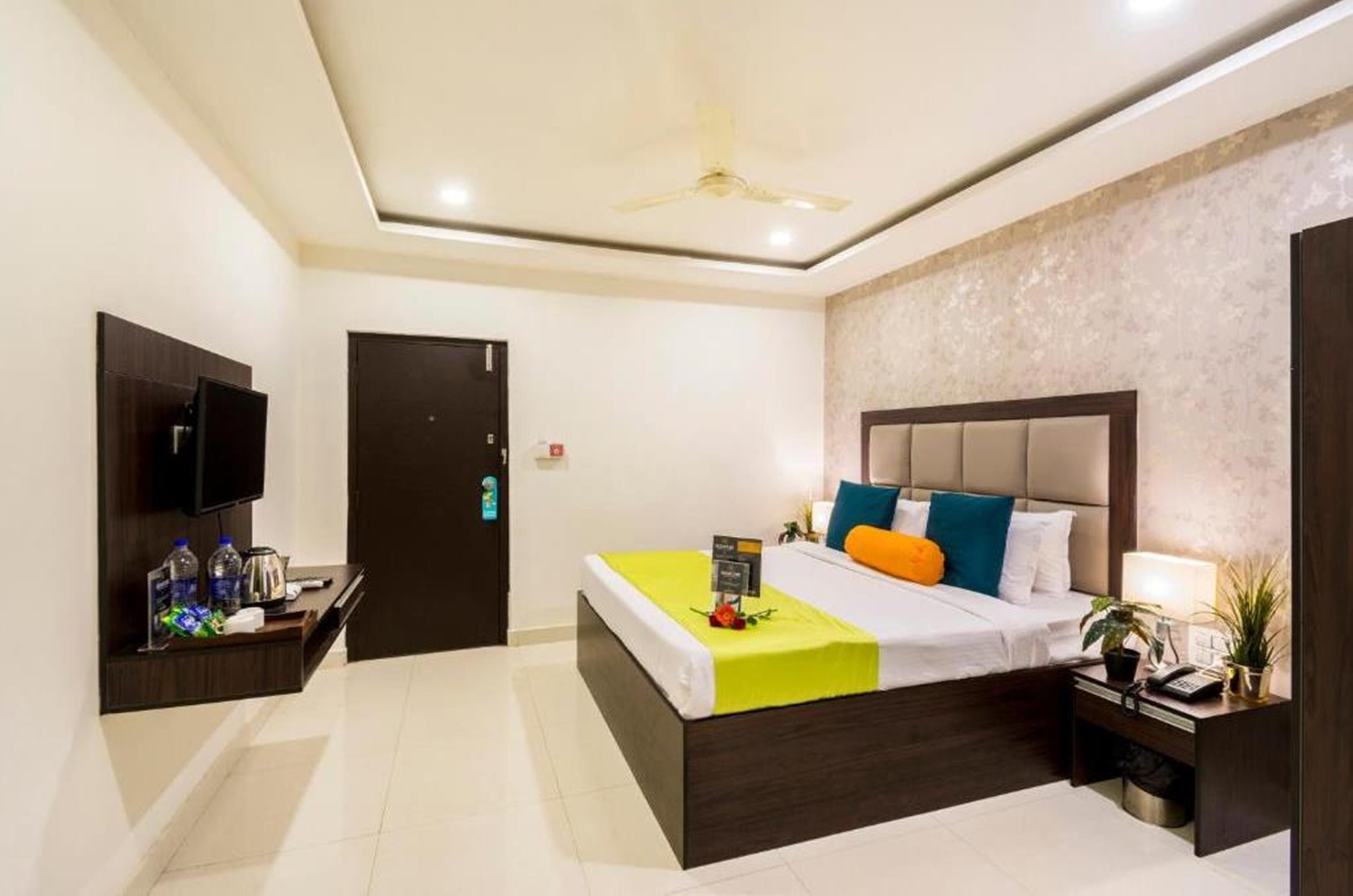A modern hotel room with a bed, bedside table, nightstand, TV, and a ceiling fan.