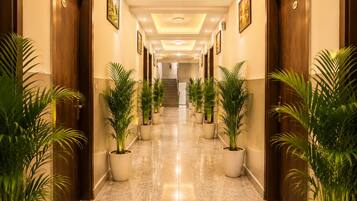 Un pasillo de hotel con piso pulido, plantas en macetas, puertas de madera y cuadros en las paredes.