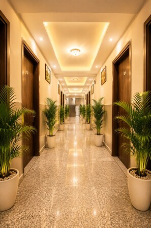 A hotel corridor with a polished floor, potted plants, wooden doors, and framed artwork on the walls. - Hotel Red Velvet Suites (New Delhi)