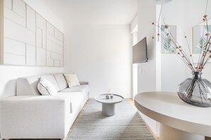 Una sala moderna con un sofá, una mesa de centro redonda, un televisor de pantalla plana y un jarrón decorativo.