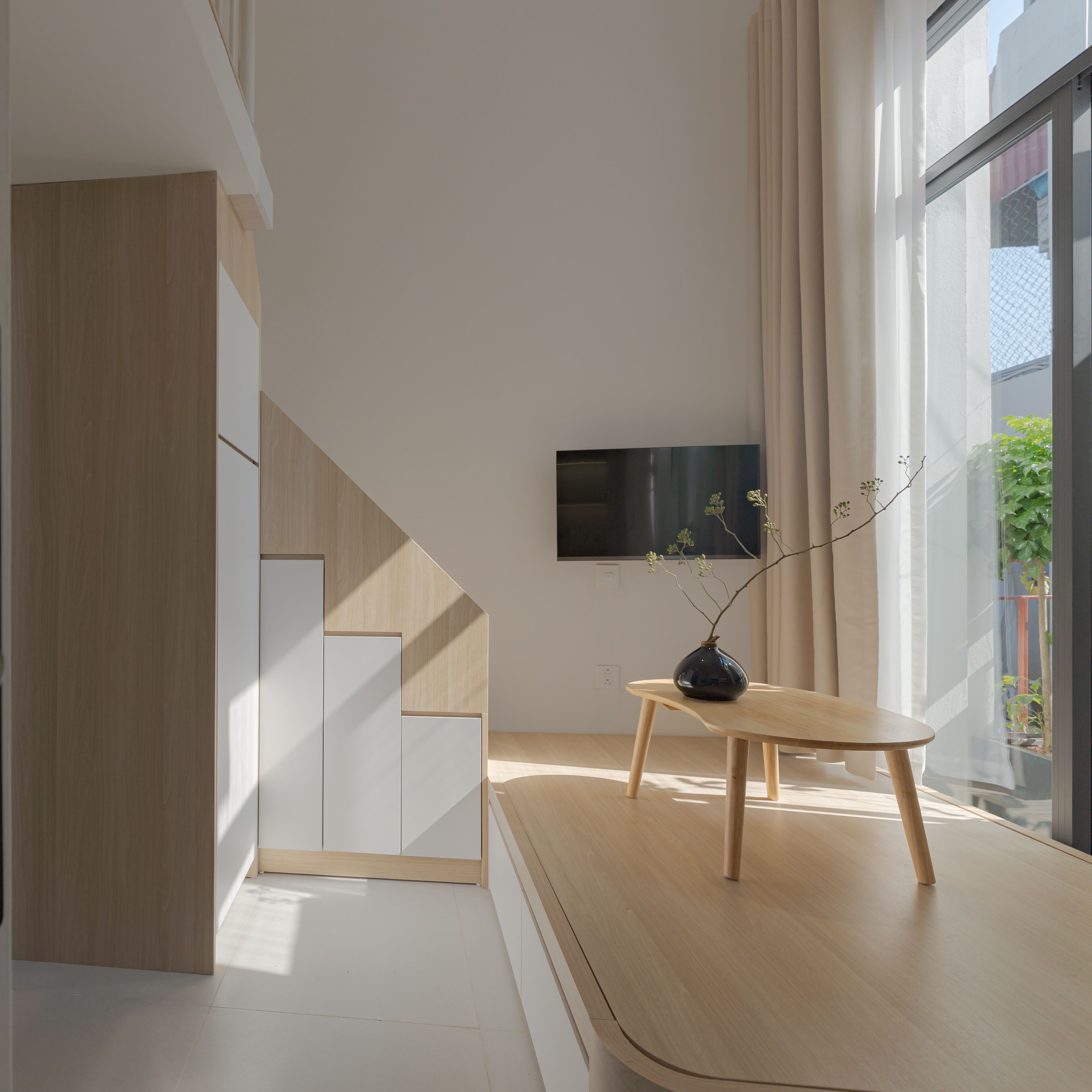 Un interior moderno con un escritorio de madera, un florero con ramas y un televisor en la pared.