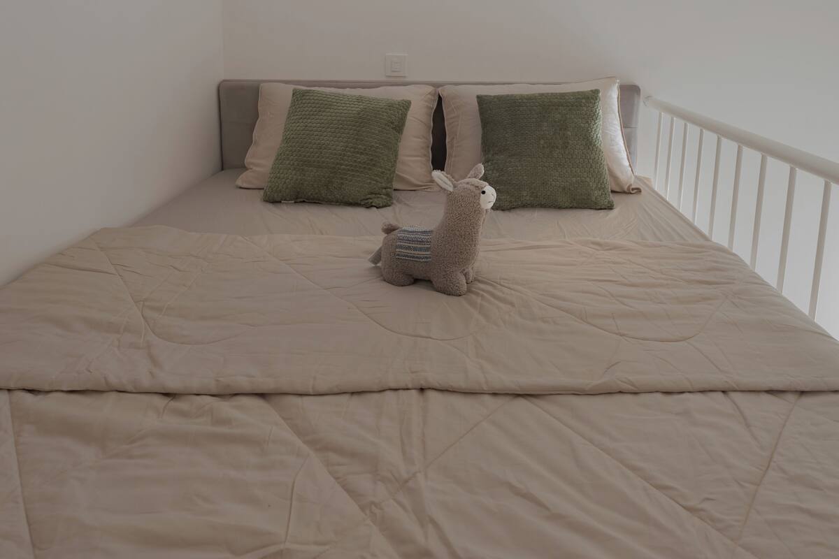 Uma cama com um edredom bege, duas almofadas e um bicho de pelúcia.