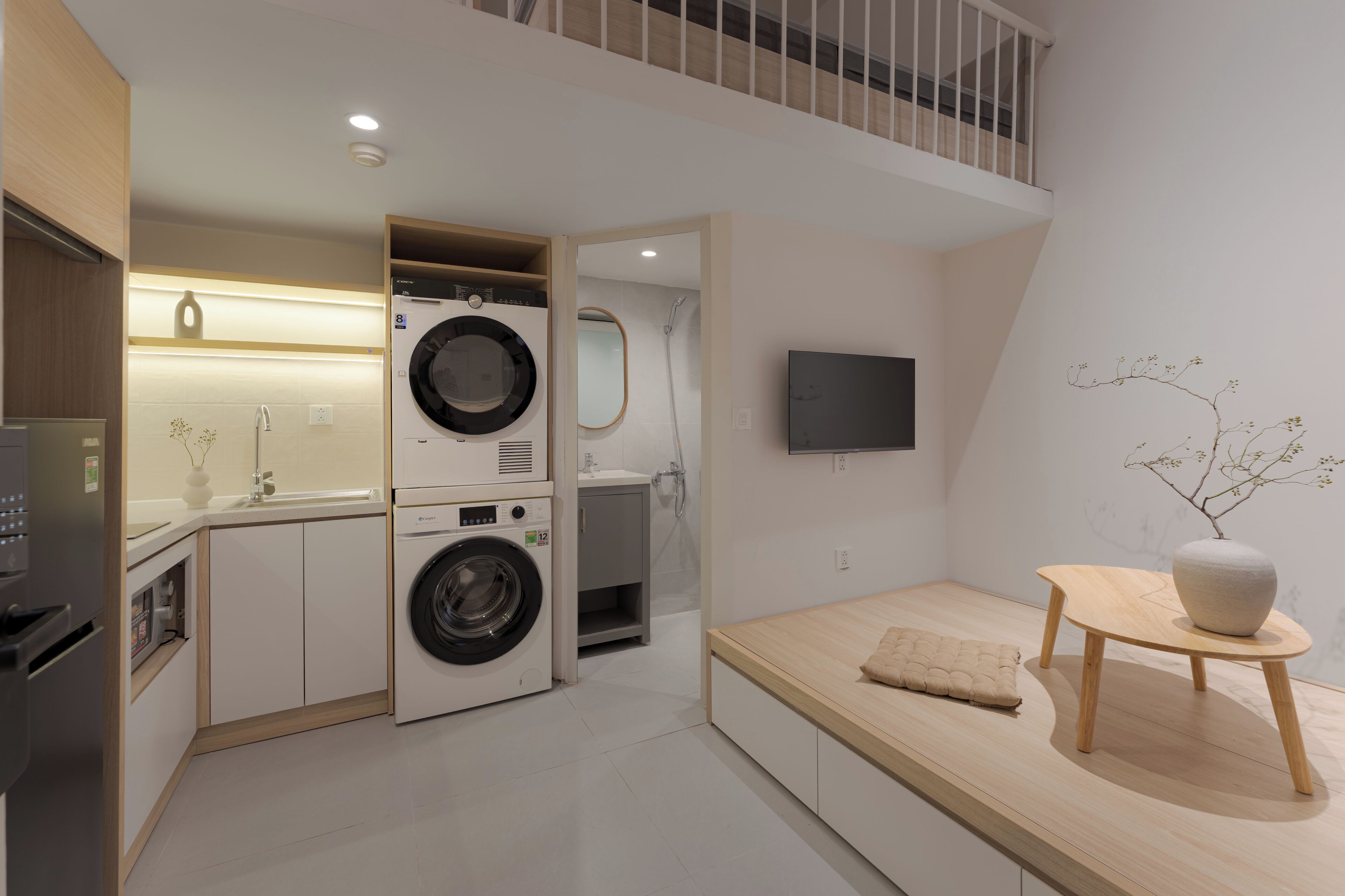 A compact kitchen with a washing machine, a sink, and a dining area with a table and a vase.
