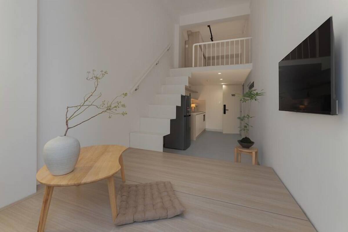 Um interior moderno com uma escada, uma sala de jantar com mesa e cadeiras, e uma sala de estar com uma televisão na parede.