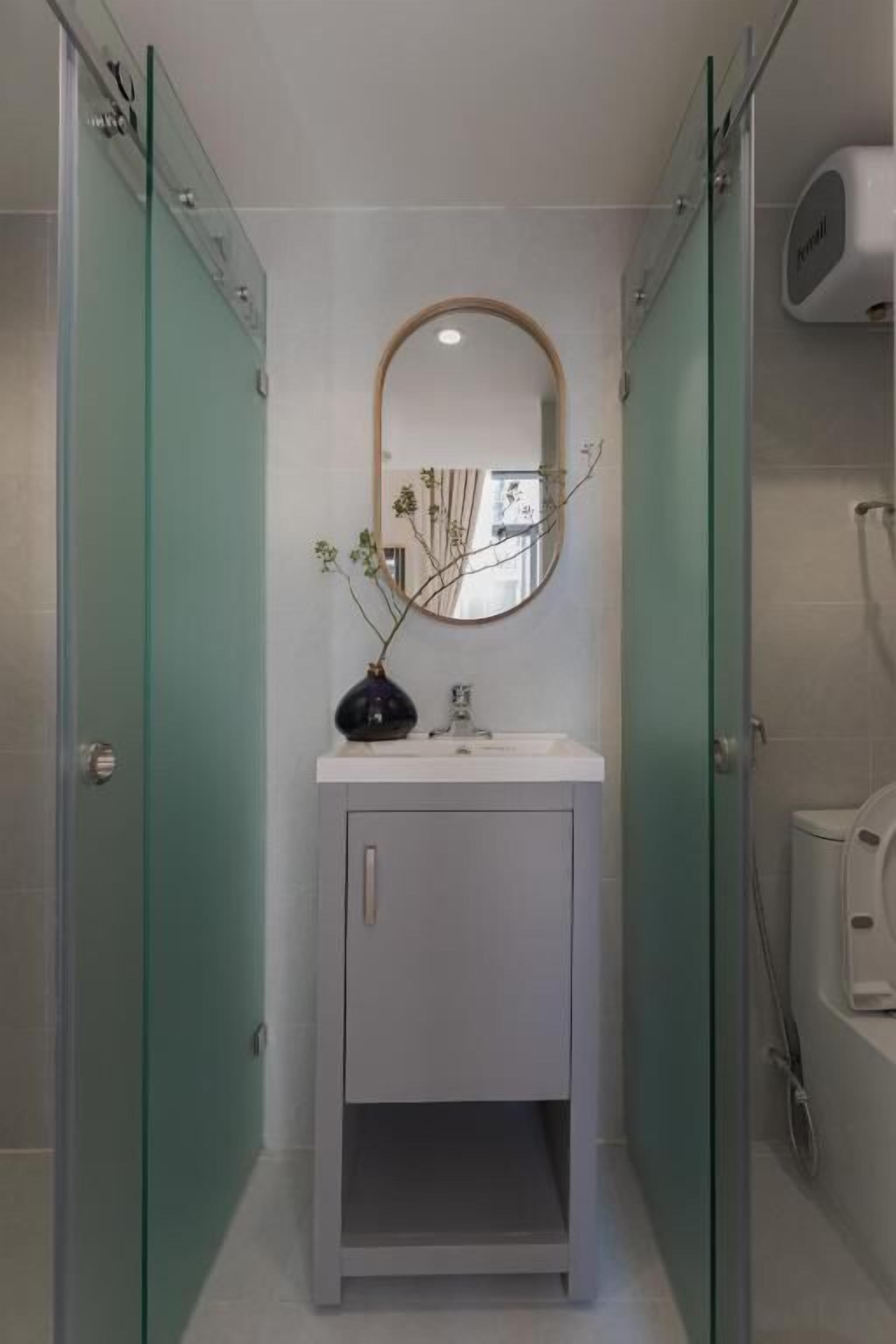 A narrow bathroom with a white vanity, a mirror, and a vase with branches.