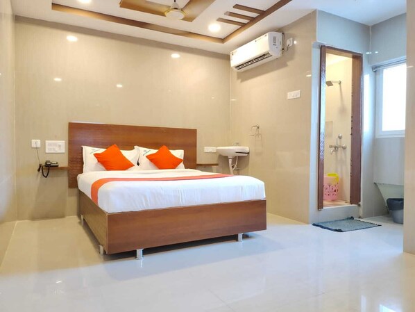 A modern hotel room with a large bed, a shower, and a built-in air conditioning unit.