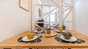A dining table set with bowls, plates, and cutlery in a modern interior with white beams and a view to a living area. - Charming 2 Bedroom Apartment at Bairro Alto (Lisboa)