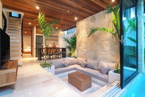 Ein modernes Interieur mit einer Steinwand, einer Holzbalkendecke, einer Couch, einem Couchtisch und einem Essbereich.