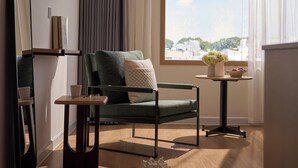Una habitación moderna con una silla verde, una mesita, un espejo y una ventana con vistas a edificios.