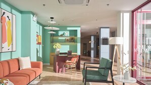 Un moderno vestíbulo de hotel con una pared de acento color turquesa, un mostrador de recepción, un sofá, una silla y una mesa de centro.