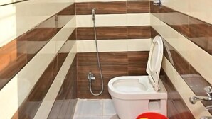 A small bathroom with a toilet, shower, and a red bucket on the floor.