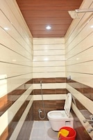 Un baño pequeño con inodoro, ducha y un balde rojo en el suelo.